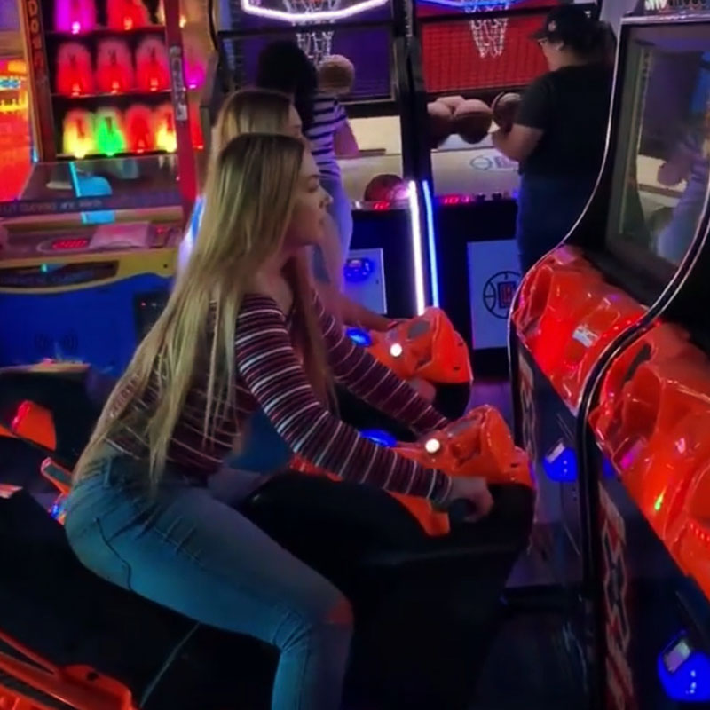 Two girls playing arcade games in a colorful game room.